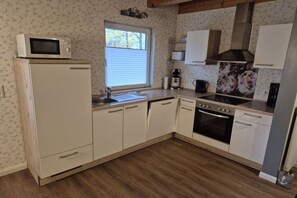 A compact kitchen with a microwave on top of a white refrigerator, a sink, a stove, and a coffee maker. - Holiday apartment with 1 bedroom (Butjadingen)