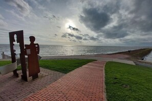 A paved walkway leading to a grassy area with a sculpture of a human figure. - Holiday apartment with 1 bedroom (Butjadingen)