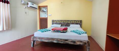 A single-bed room with a wooden headboard, a red and white striped bedspread, and a window with curtains.