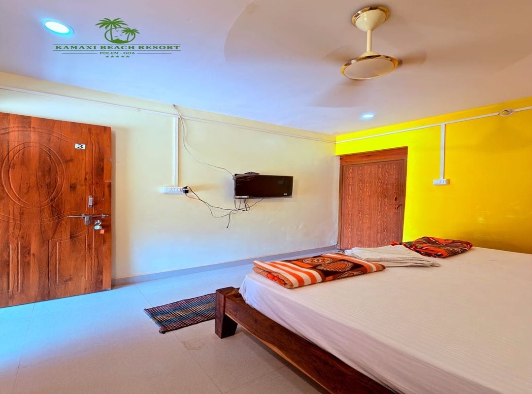 A hotel room with a bed, a television, a wooden wardrobe, and a ceiling fan.