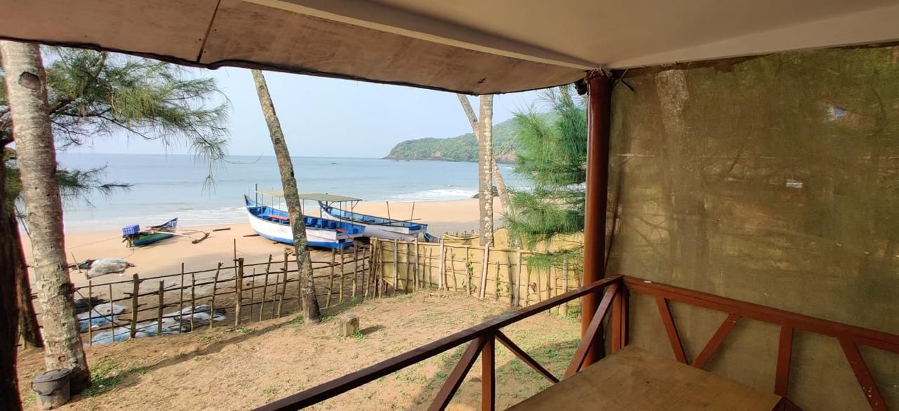 A beach view from a covered area with a wooden fence, a blue boat, and a sandy beach.