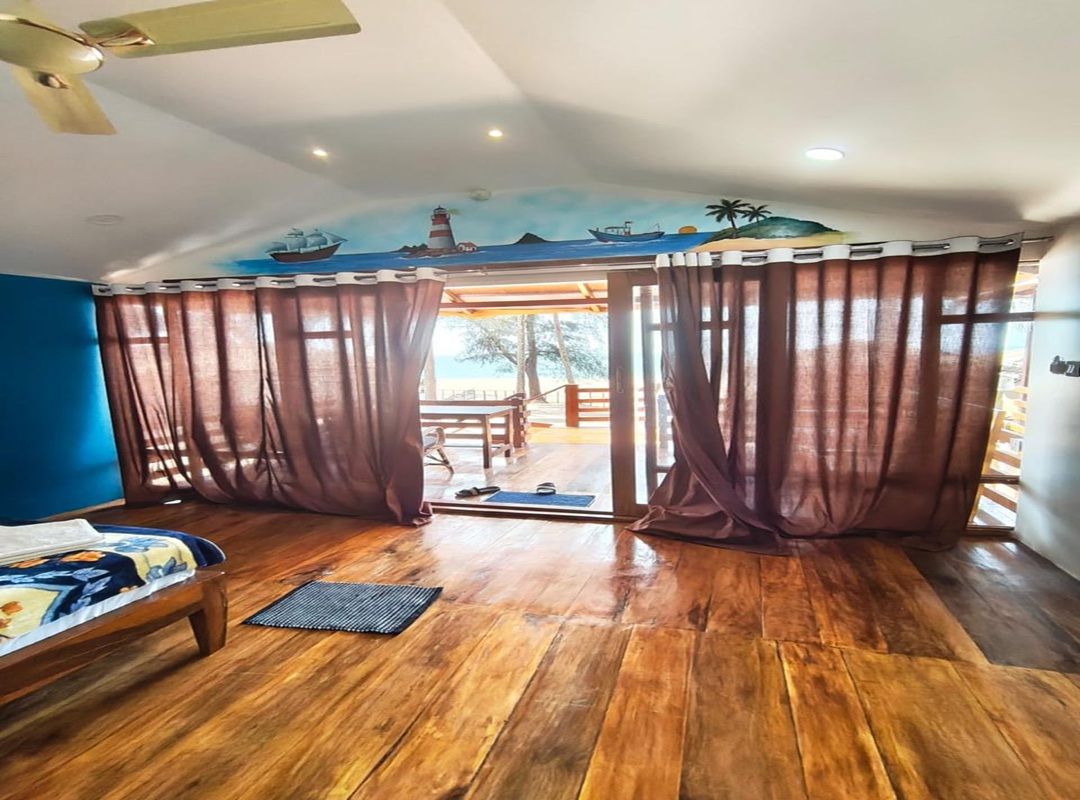 A room with a bed, a ceiling fan, and a view through a curtain to an outdoor area.