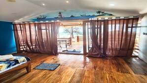 Quarto com cama, ventilador de teto e vista para área externa através de uma cortina.