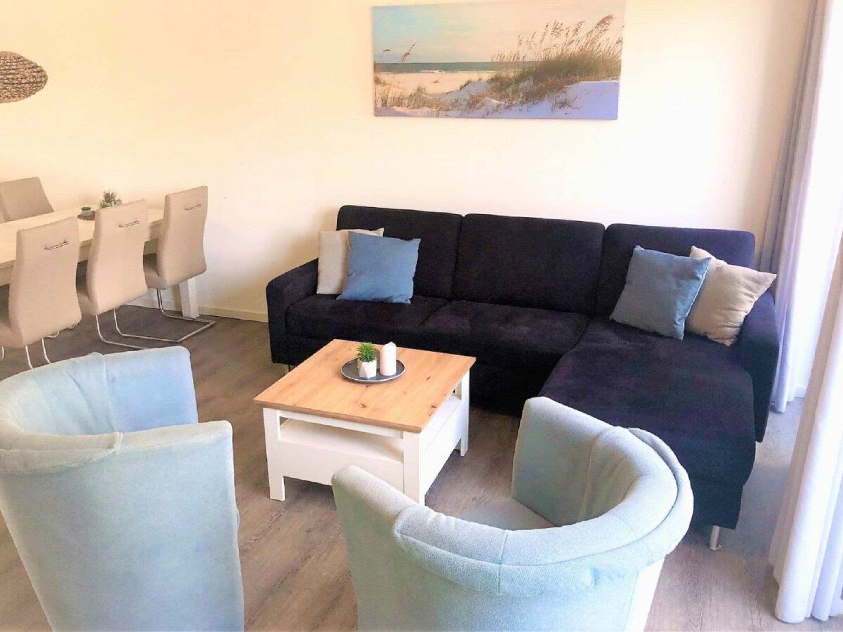 A living room with a dark-colored sofa, light-colored armchairs, a small wooden coffee table, and a painting of a beach scene on the wall.