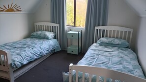 Een tweepersoonskamer met twee enkele bedden, een nachtkastje en een raam met gordijnen.
