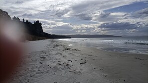 Een strand met een zandstrand, golven en een beboste heuvelrug op de achtergrond.