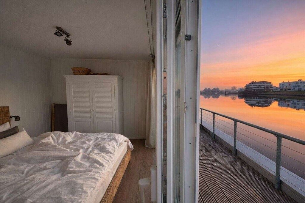 Une chambre avec un lit, une armoire et une vue sur une étendue d’eau paisible au coucher du soleil.