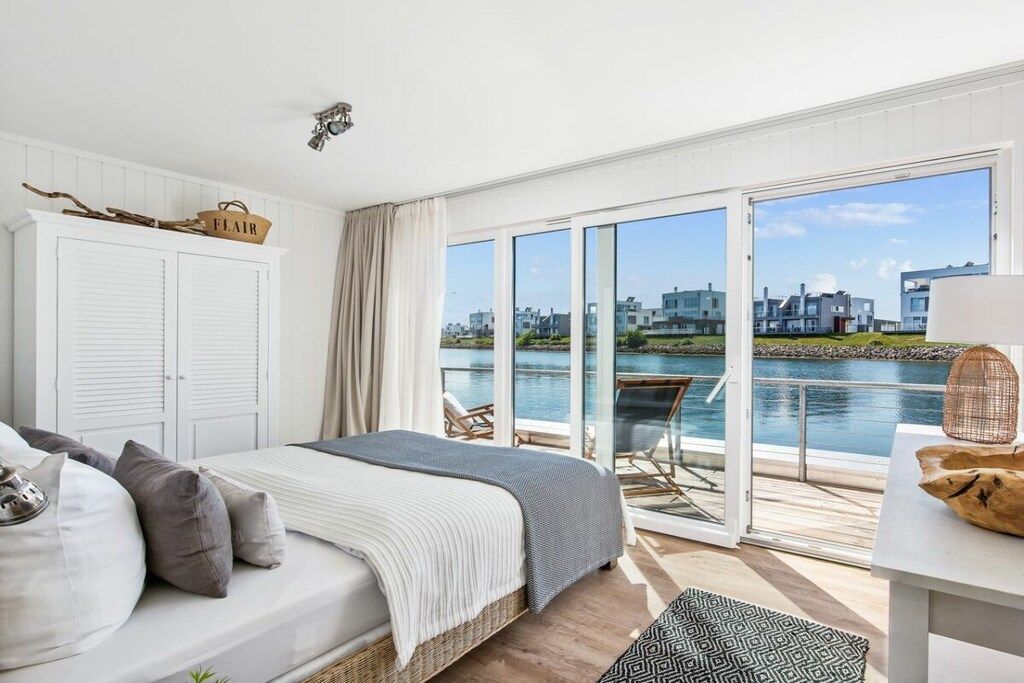 Une chambre avec un lit, une armoire, une vue sur un plan d’eau et un balcon équipé d’une table et de chaises.