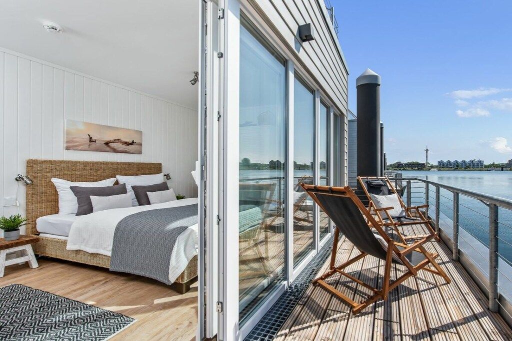 A bedroom with a large bed, a bedside table, and a view of the water through a sliding glass door.
