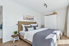 Une chambre à coucher avec un lit, un petit tabouret, une plante, un tableau et une armoire.