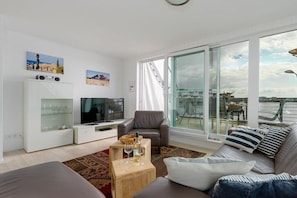 A modern living room with a television, seating, and a view of the sea.