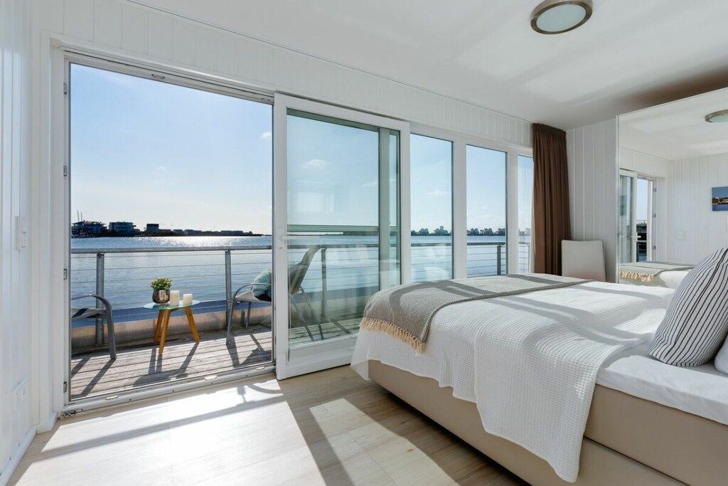 A bedroom with a large bed, a view of the water, and a balcony with chairs and a table.