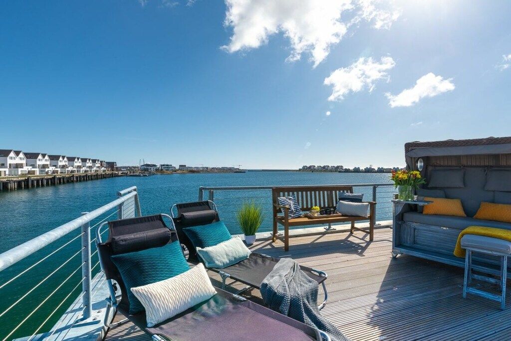 A deck with lounge chairs and a sofa overlooking a body of water with a pier in the background.