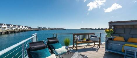 A deck with lounge chairs and a sofa overlooking a body of water with a pier in the background.