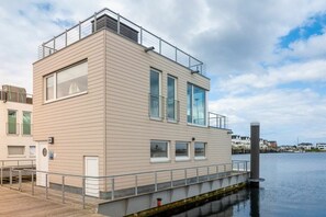 A modern building with a flat roof, large windows, and a dock extending into the water. - Houseboat in Kappeln with swimming pool (Kappeln)