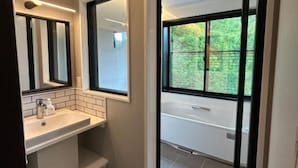 Ein Badezimmer mit schwarz-weiß kariertem Boden, einem weißen Waschbecken und einem großen Fenster mit Blick auf Grünflächen.