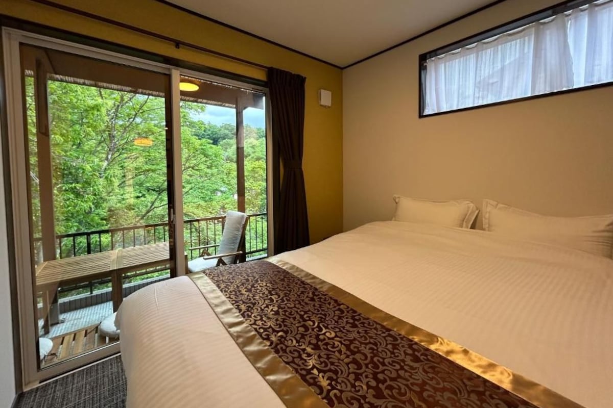Habitación de hotel con una cama grande, un balcón con una silla y vistas a zonas verdes.