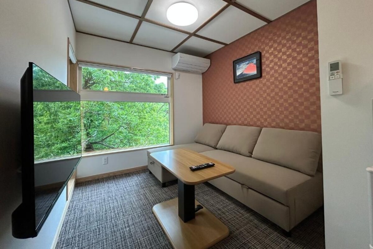 Una habitación con sofá, una mesita, televisión y ventana con vista a zonas verdes.