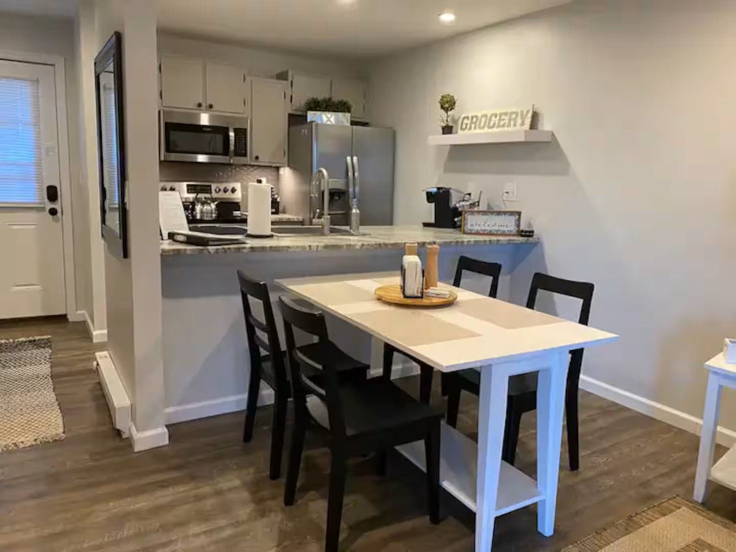 Una cocina moderna con zona de comedor, que incluye un microondas, refrigerador y un letrero en la pared que dice 'GROCERY'.