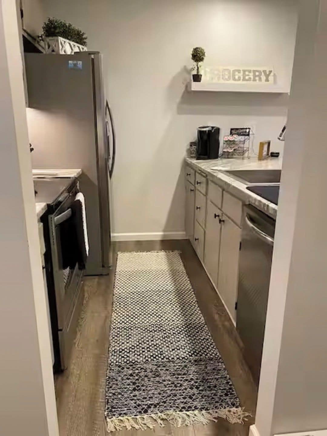 A narrow kitchen with a refrigerator, cabinets, and a sink.