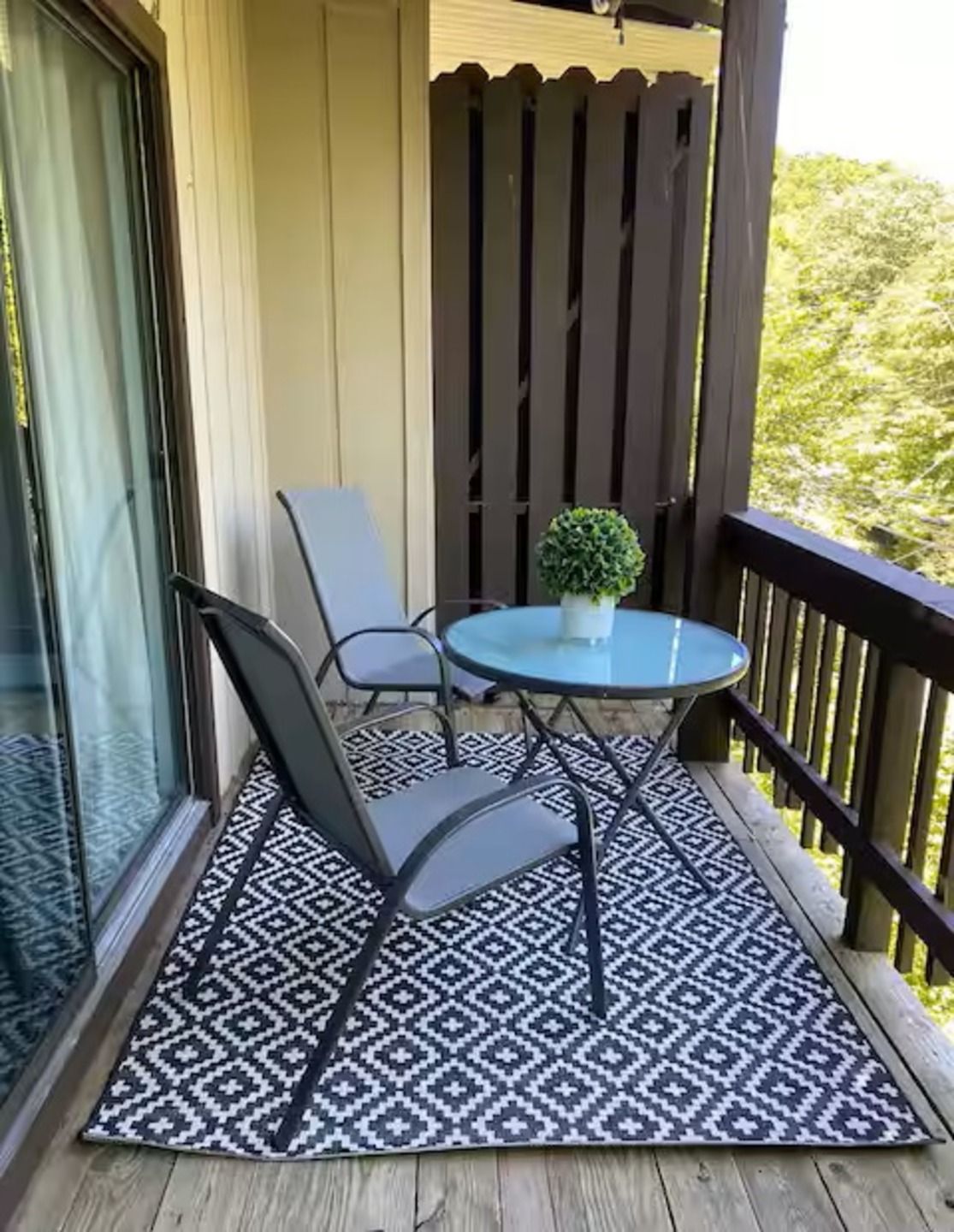 Un balcon avec une table et deux chaises, une plante en pot et un tapis à motifs.