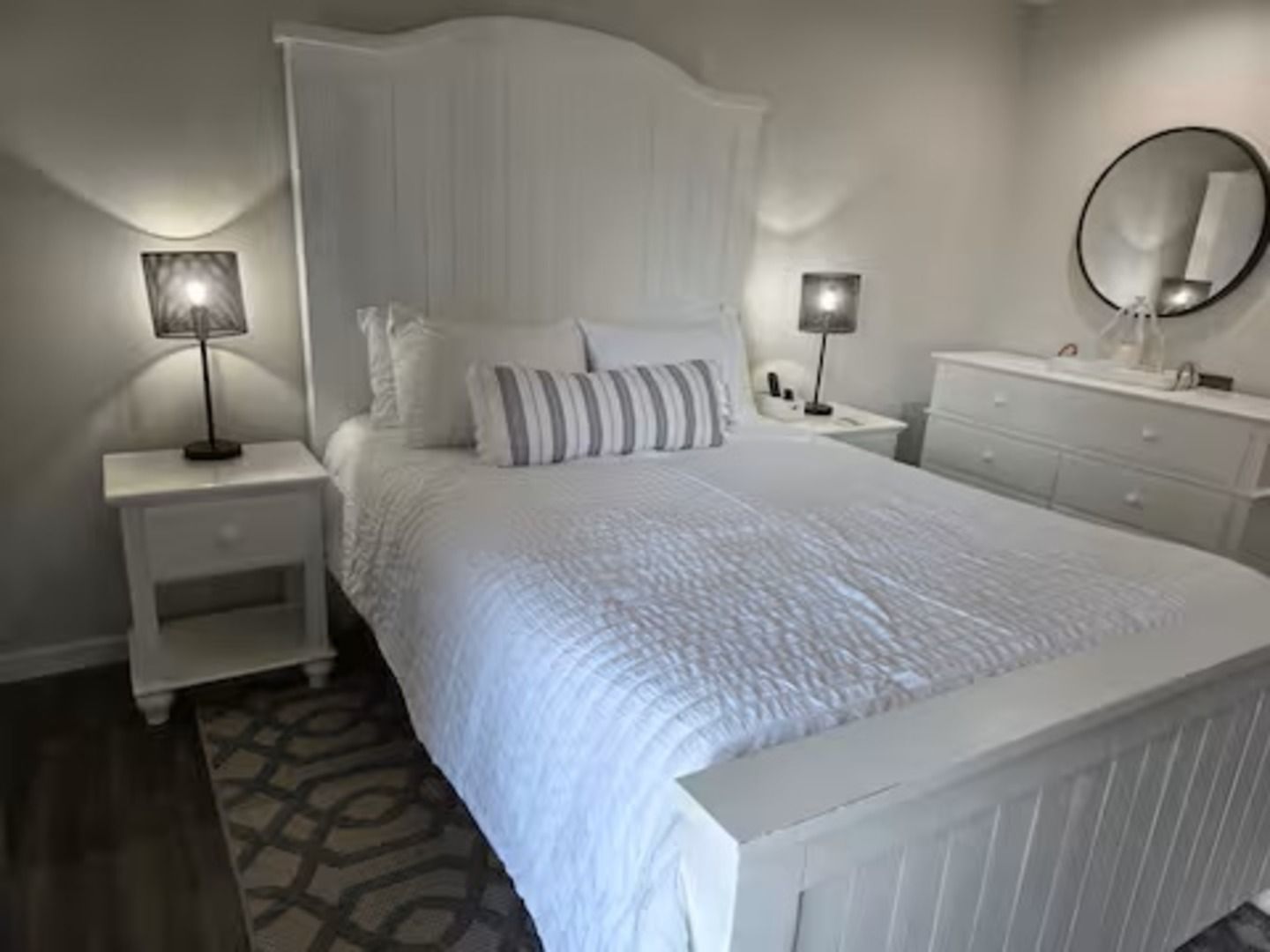 Un dormitorio con una cama grande, dos mesitas de noche, un aparador y un espejo.