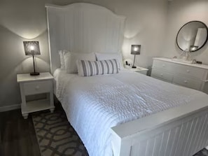 Un dormitorio con una cama grande, dos mesitas de noche, un aparador y un espejo.