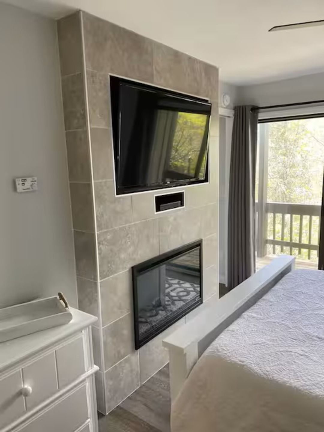 A modern bedroom with a large bed, a television mounted on the wall, and a fireplace.
