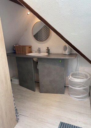 Ein modernes Badezimmer mit integriertem Waschbecken, einem Holzkästen und einem runden Spiegel.