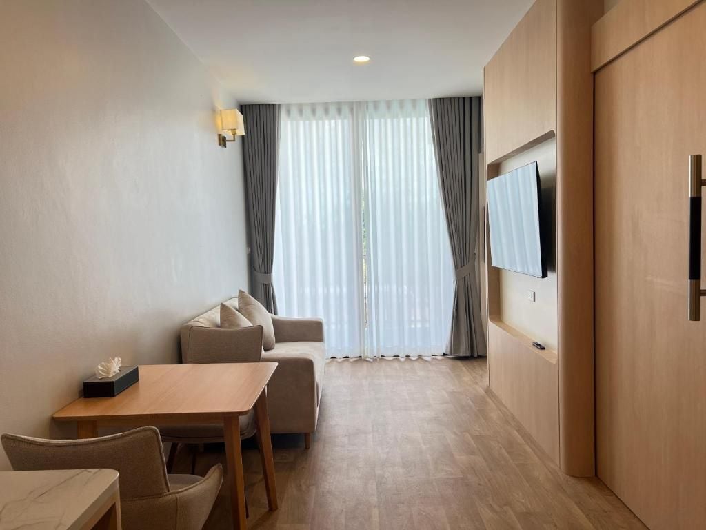 Habitación de hotel con sofá, mesa de comedor, sillas, televisor de pantalla plana montado en la pared y puerta corrediza que da a un balcón.