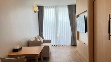 Habitación de hotel con sofá, mesa de comedor, sillas, televisor de pantalla plana montado en la pared y puerta corrediza que da a un balcón.