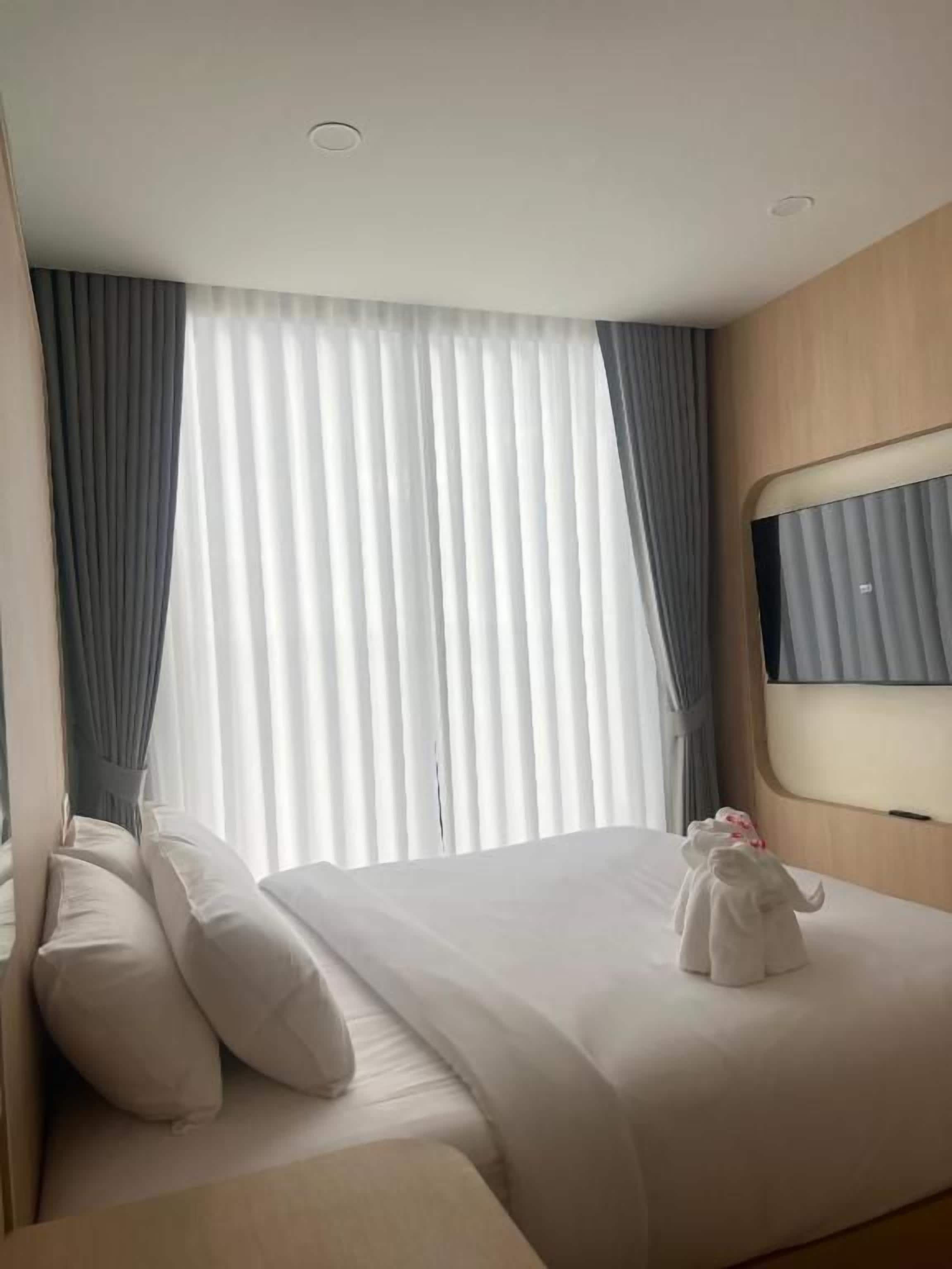 A hotel room with a bed, a bedside table, a flat-screen TV, and a window with curtains.