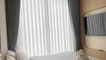 A hotel room with a bed, a bedside table, a flat-screen TV, and a window with curtains.