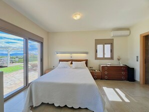 A bedroom with a large bed, a nightstand, a dresser, and a window with a view of the outdoors. - Villa Artemis, Tolo, Nafplio (Tolo)