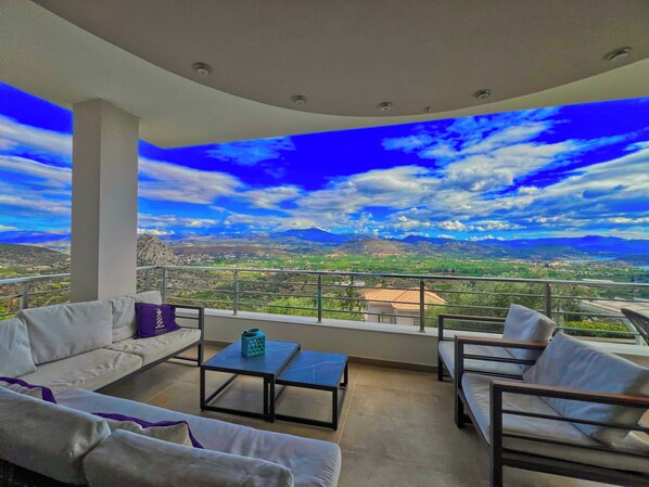 A balcony with a white sofa, a small table, and a view of a mountainous landscape. - Villa Artemis, Tolo, Nafplio (Tolo)