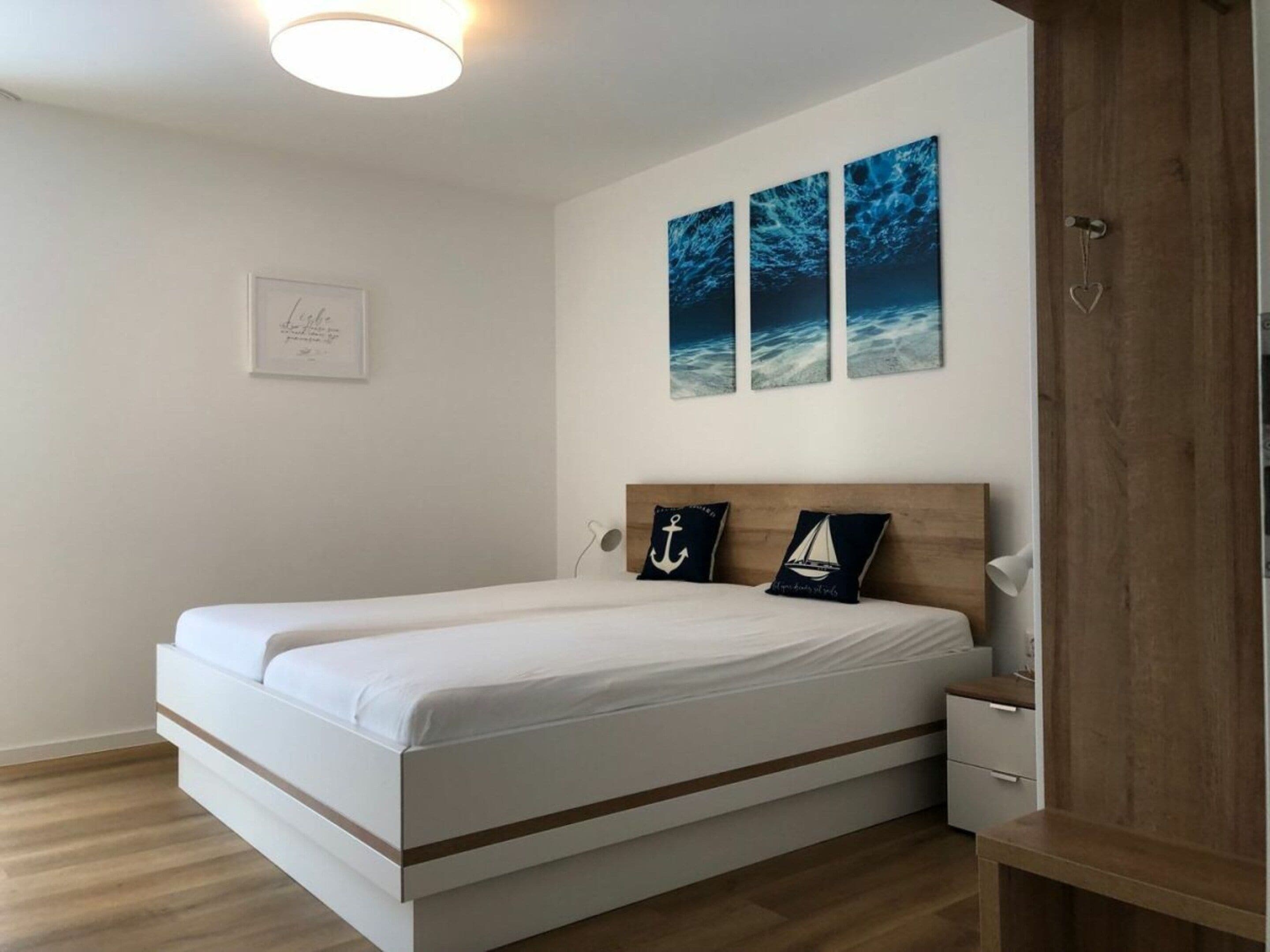 A modern bedroom with a bed, a bedside table, and a nightstand. There are three wall-mounted artworks above the bed.