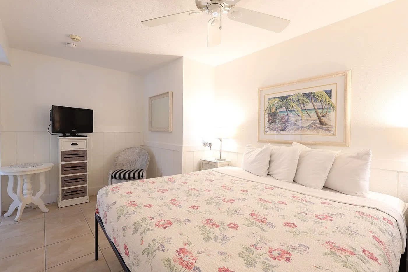 Une chambre à coucher avec un lit, une télévision, une chaise, une petite table et un tableau accroché au mur.