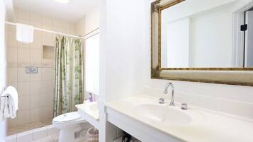 A bathroom with a shower, toilet, sink, and a mirror with a gold frame.