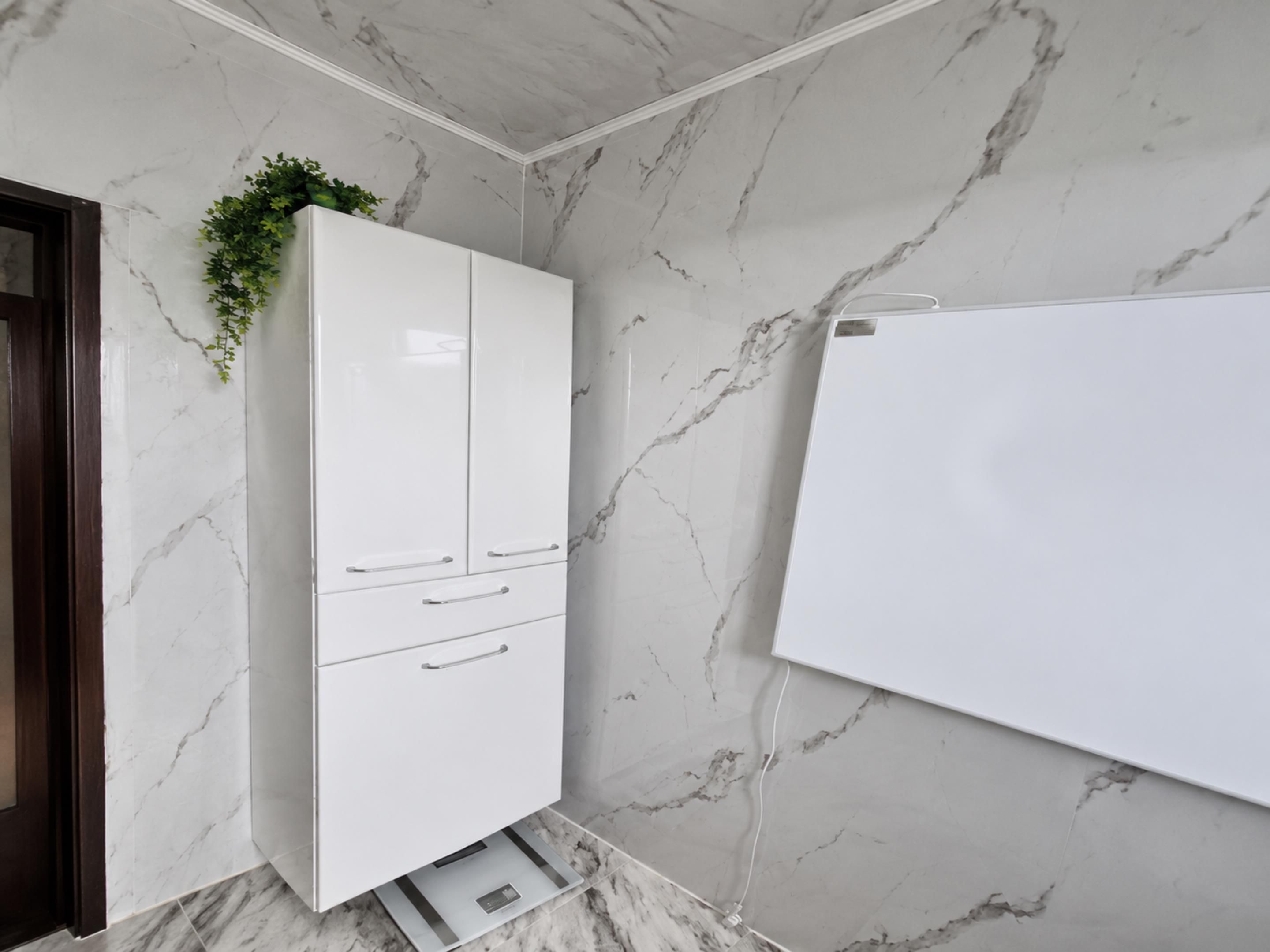 A bathroom with a white cabinet, marble walls, and a whiteboard.