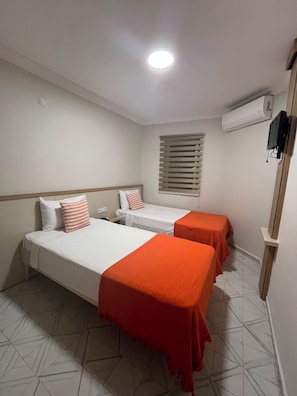 A hotel room with two beds, a window with blinds, an air conditioning unit, and a television mounted on the wall. - Deniz 61 Otel (Bodrum)