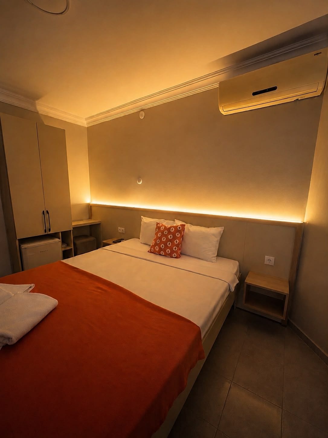Quarto de hotel com cama, mesa de cabeceira, guarda-roupa e ar condicionado.