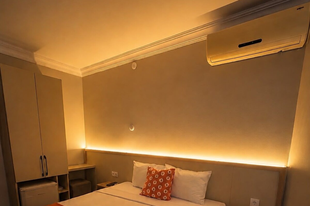 Una habitación de hotel con una cama, una mesita de noche, un armario y un equipo de aire acondicionado.