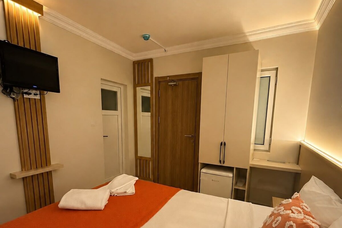 Habitación de hotel con cama, televisor montado en la pared, puerta de madera y una pequeña kitchenette.
