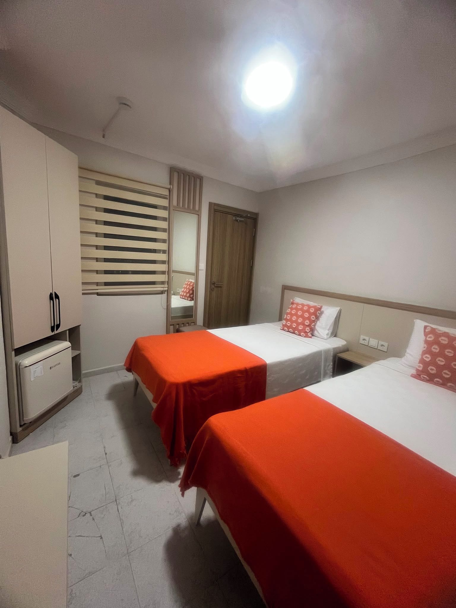 A hotel room with two beds, a wardrobe, a mirror, and a window with blinds.