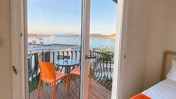 Ein Hotelzimmer mit Balkon, einem Bett mit orangefarbener Decke und Blick auf das Meer und Boote.