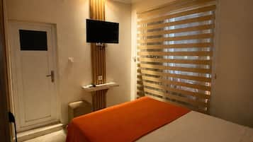 A hotel room with a bed, a television mounted on the wall, a window with blinds, and a door.