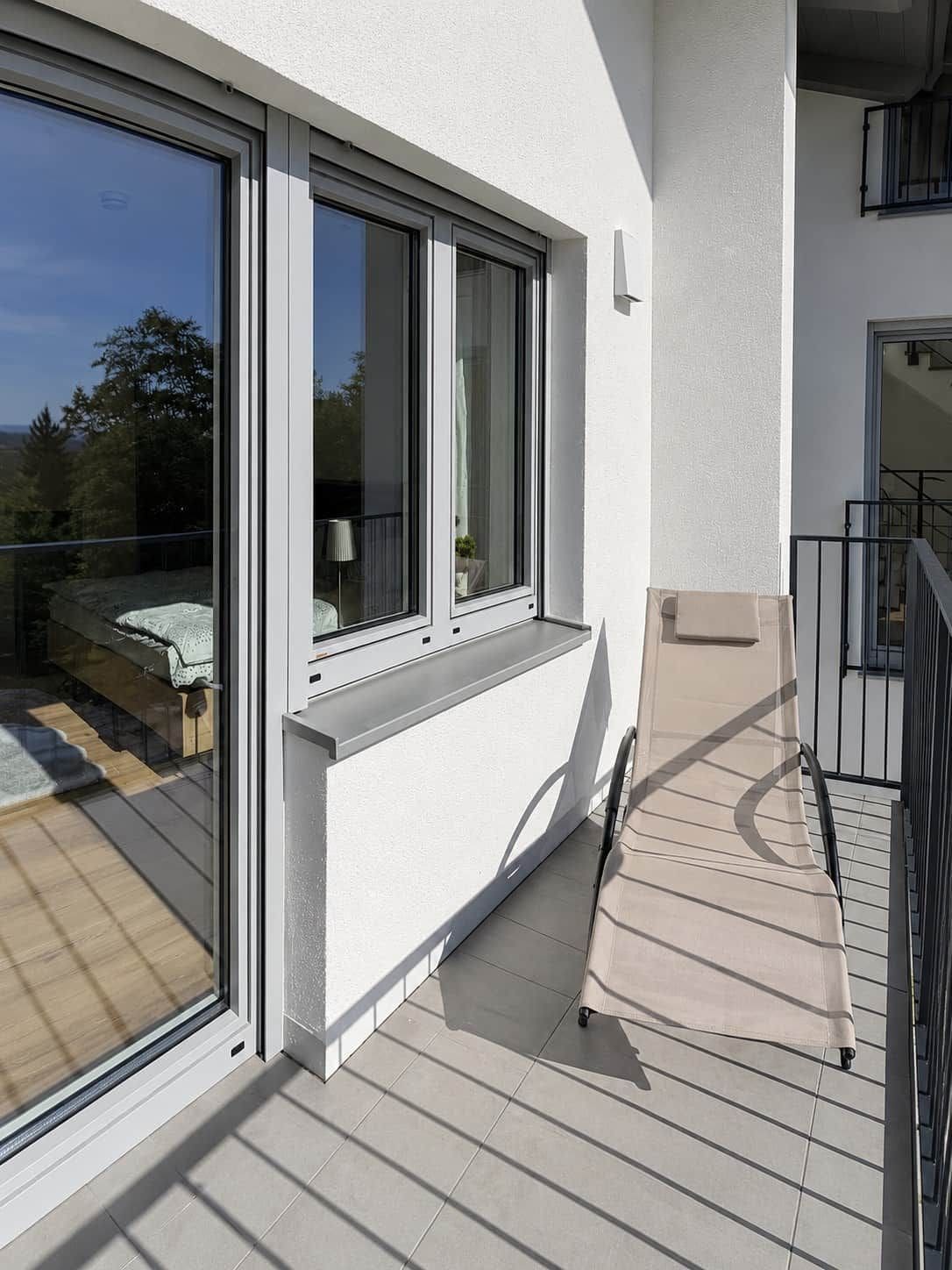A balcony with a glass door, a white exterior wall, and a tiled floor.