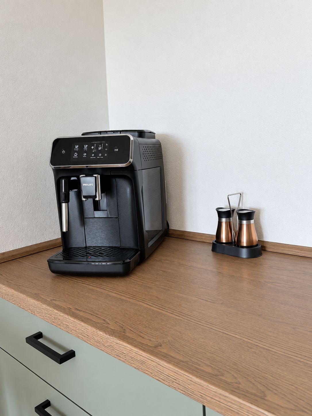 Une machine à café est posée sur un plan de travail en bois, à côté se trouvent un moulin à café et deux récipients.