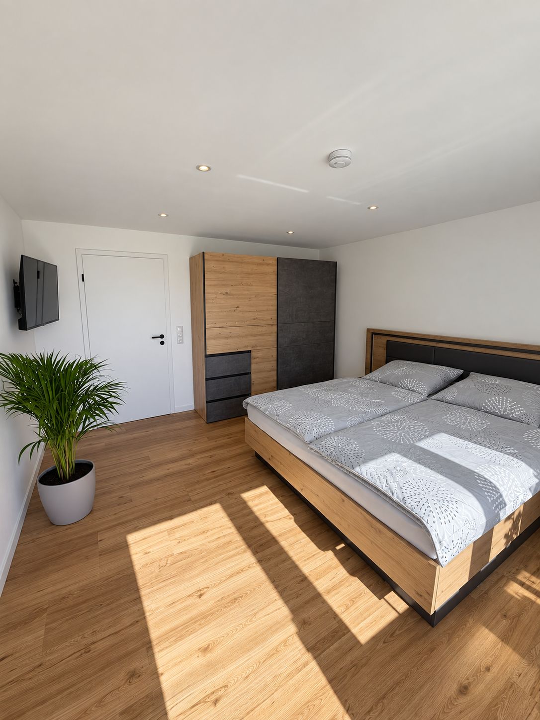 A modern bedroom with a wooden bed, a potted plant, and built-in storage.