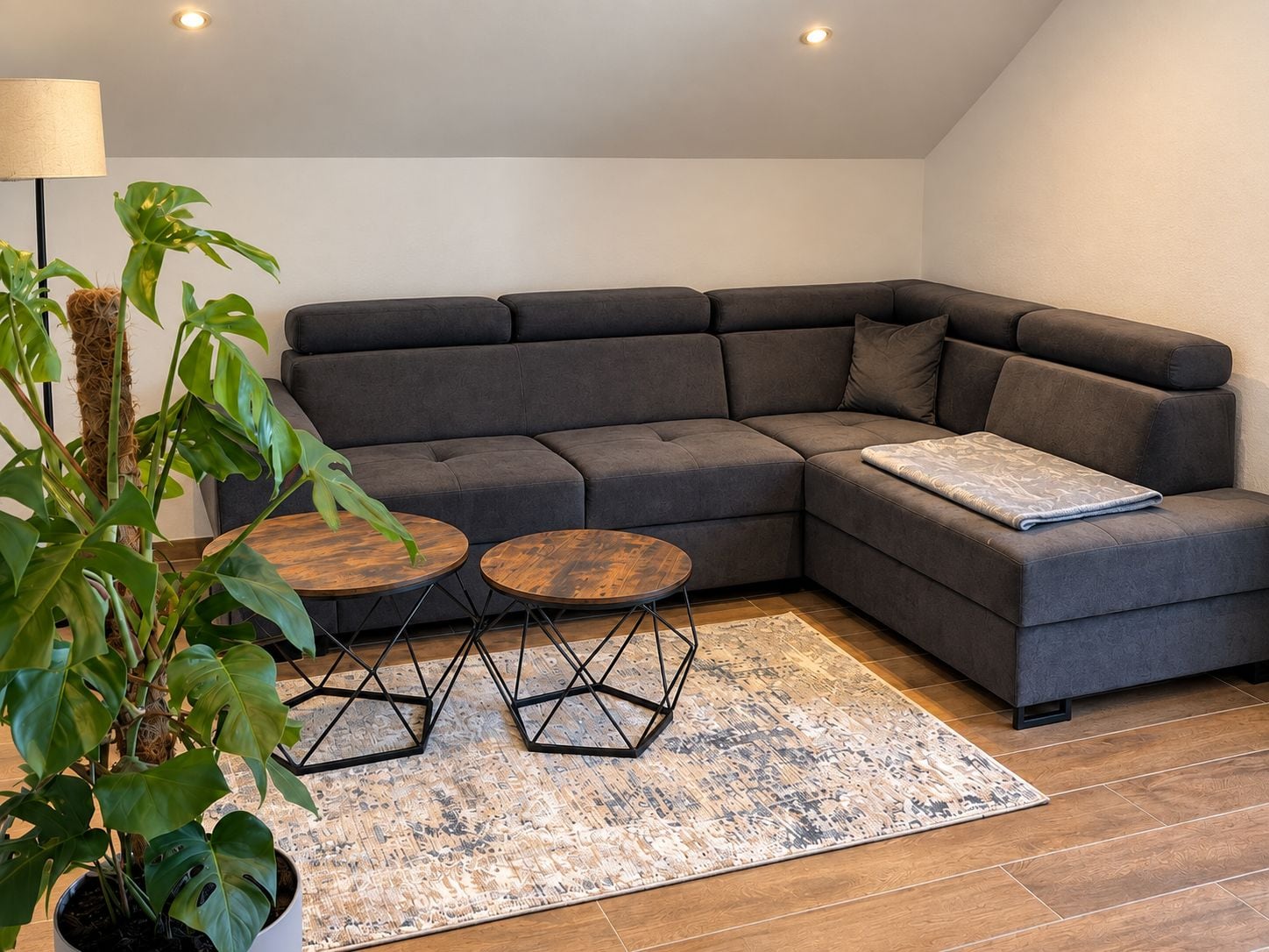Ein modernes Wohnzimmer mit einer Eckcouch, zwei runden Holztischen und einer großen Kühlpflanze.